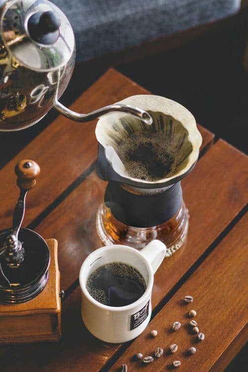 A person with a coffee pot pours Peaberry Kona Coffee into a mug.